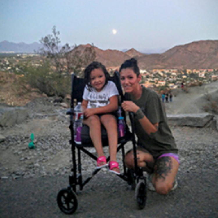Jacqulyn squatting next to her daughter Layla who is in her wheelchair