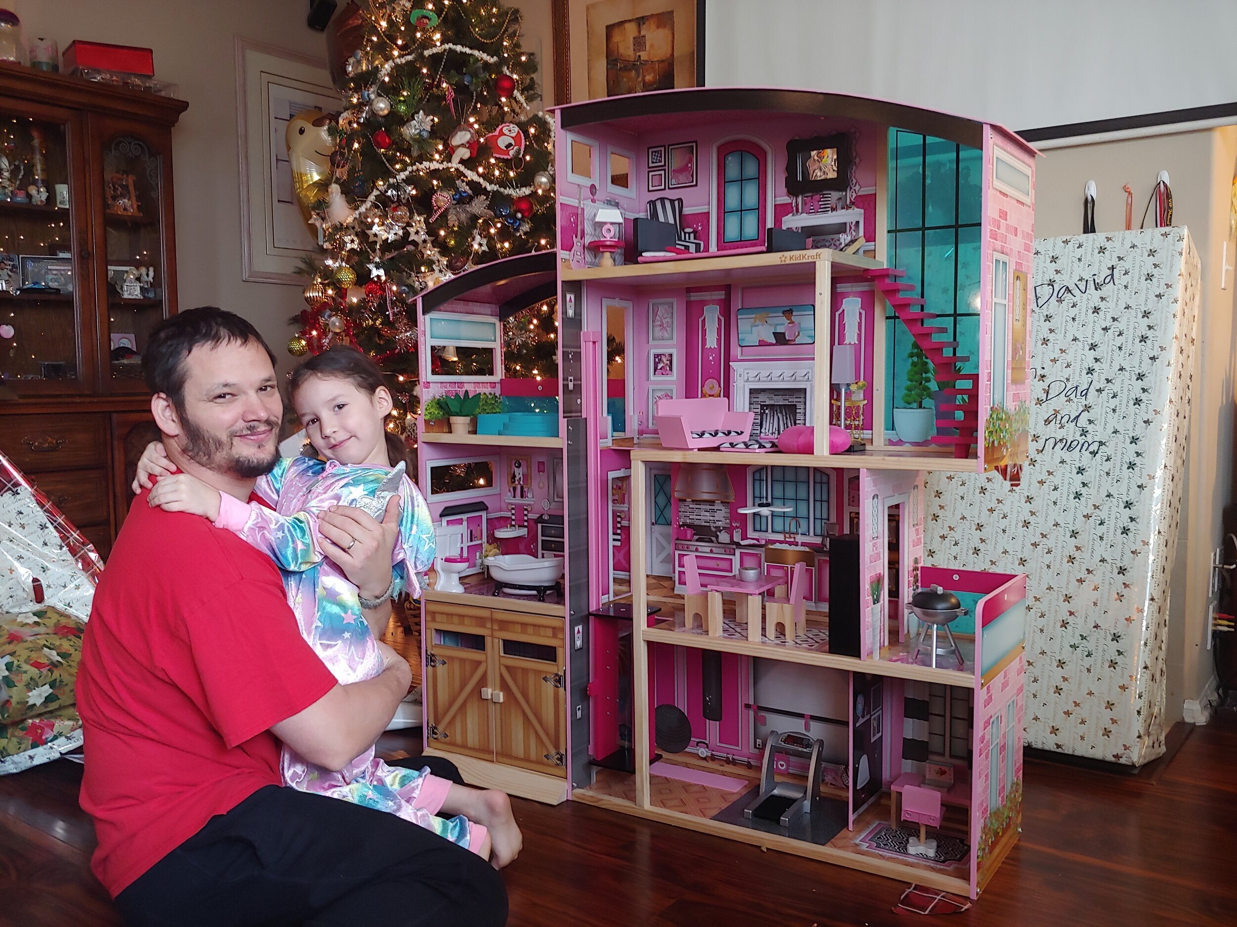 A dad hugging his daughter in front of the new doll house she just got as a present