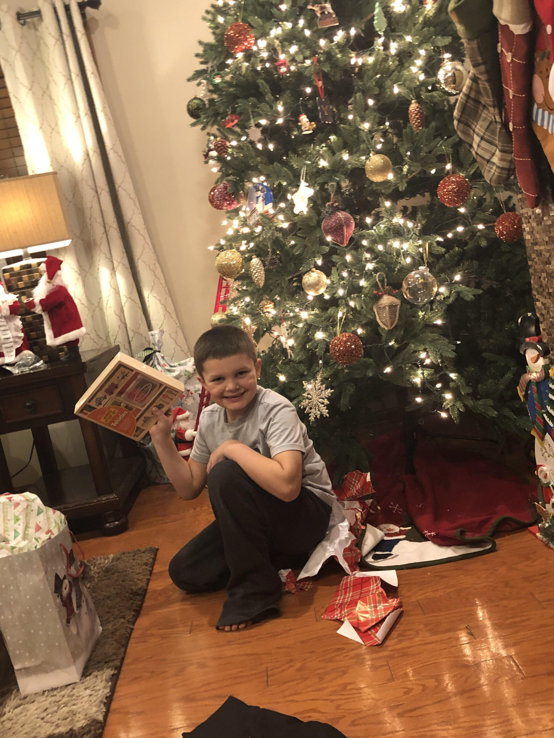 A boy smiling in front of a Christmas tree with his new present